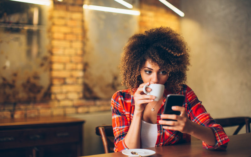Young Woman At Cafe Drinking Coffee And Using Mobile Phone