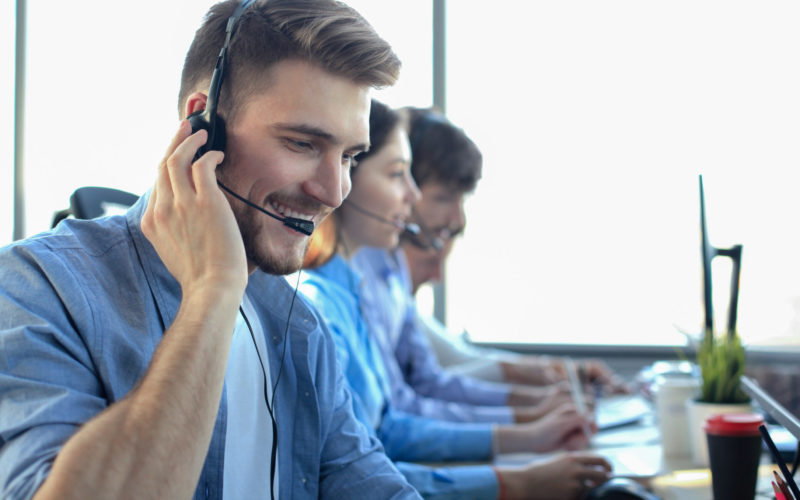Portrait Of Call Center Worker Accompanied By His Team. Smiling Customer Support Operator At Work.